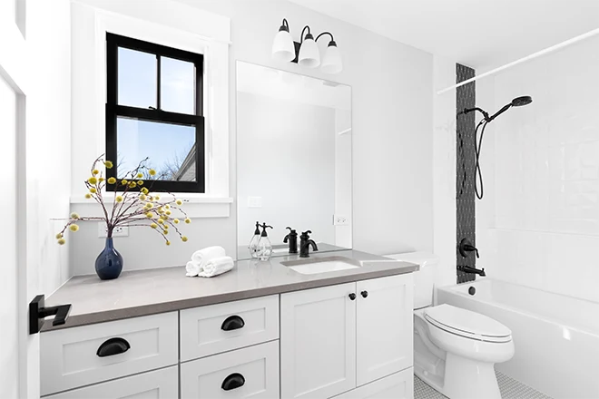 A luxury renovated white bathroom with a brown granite countertop, black hardware and faucets, and a custom tiled shower