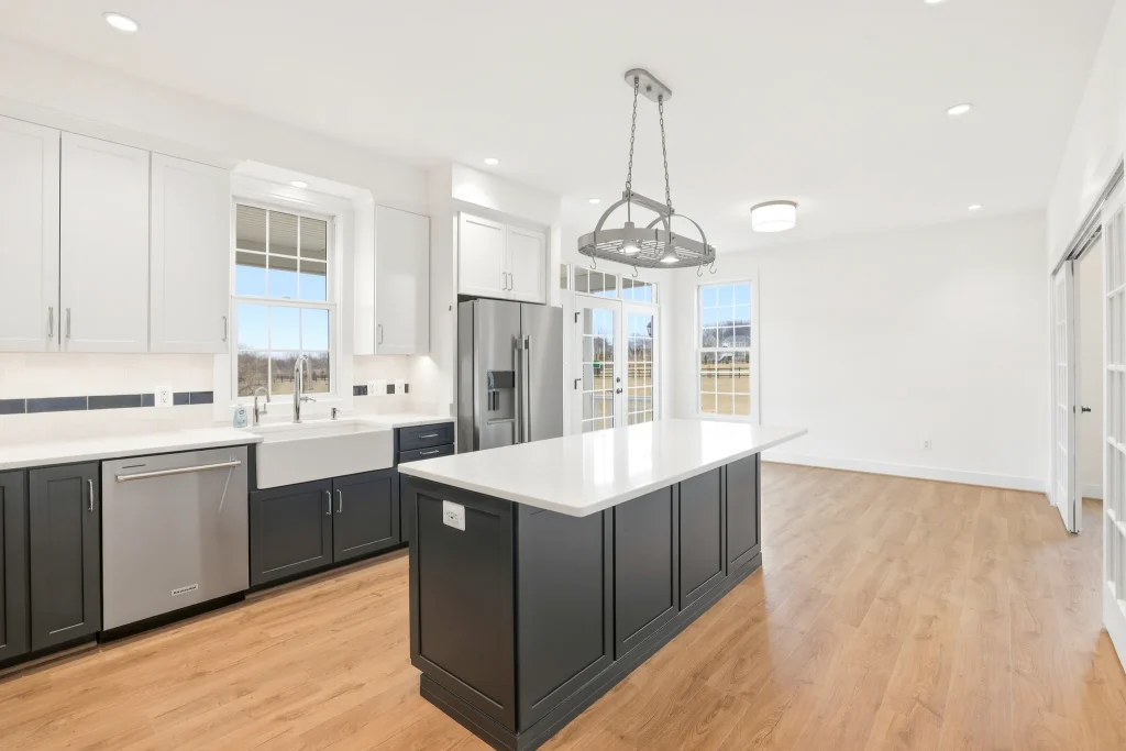 Bright, modern kitchen with white upper cabinets, dark island base, stainless-steel appliances, and large windows letting in daylight.