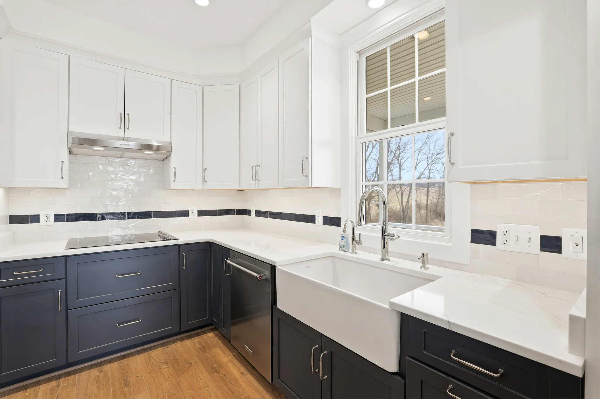 Modern kitchen with white upper cabinets, navy lower cabinets, stainless steel appliances, and a large window above the sink.