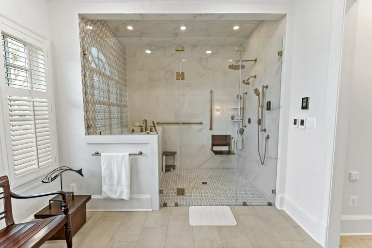 Bright marble bathroom with a glass shower enclosure, gold fixtures, and white window shutters.